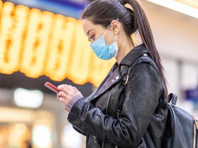 Woman with mask and cell phone at train station