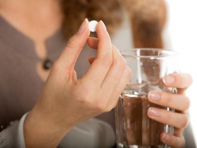 Woman holding white pill and glass of water