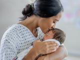 A mother holds her newborn and kisses the baby's head.