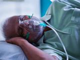 Older man wearing oxygen mask, lying on his side