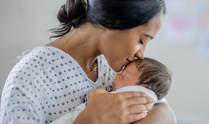 A mother holds her newborn and kisses the baby's head.