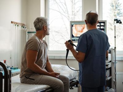 Doctor explaining colonoscopy results to older White man who is sitting on exam table