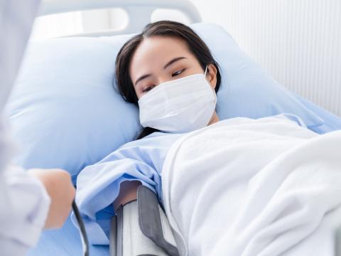 Woman in hospital bed getting blood pressure checked