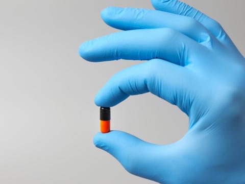 Black and orange capsule in gloved hand