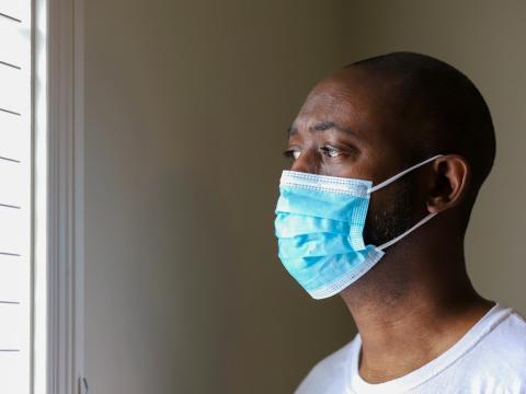 Black man wearing mask looks out window