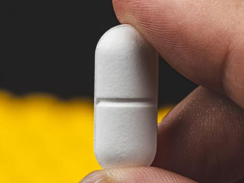 Closeup of fingers holding a white pill