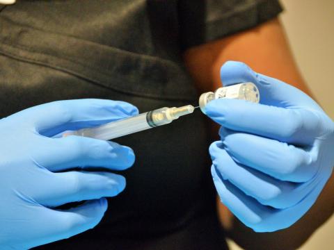 Gloved hands drawing COVID vaccine into syringe