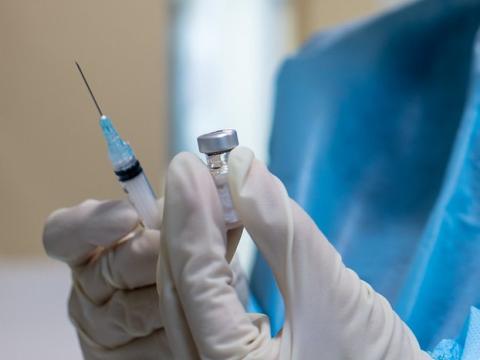 Gloved hands holding COVID vaccine vial and syringe