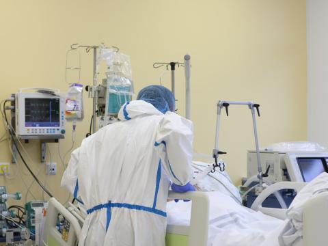 Healthcare worker bending over COVID patient's bed