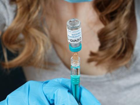 Health worker holding COVID vaccine vial upside down with syringe