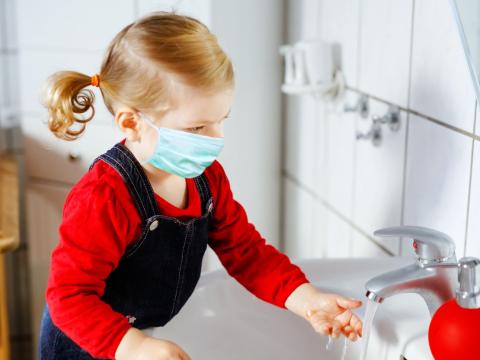 Masked preschooler washing hands