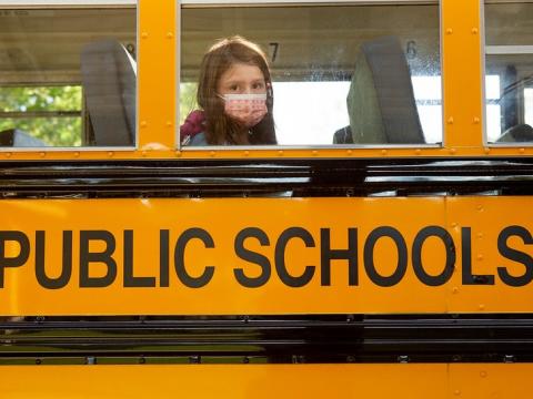 Masked schoolgirl looks out bus window