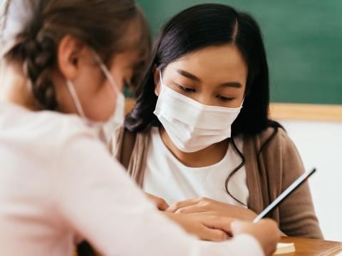 Masked teacher helping masked student