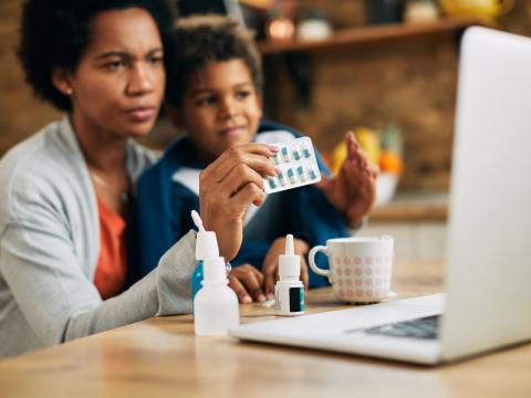 Mom holding capsules with boy at computer