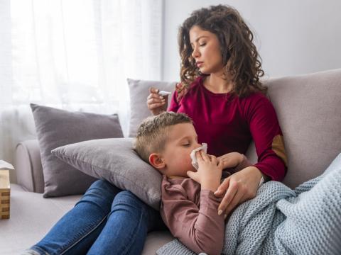 Mom taking temperature of sick boy on couch