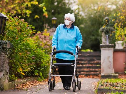 Older woman wearing mask outside using walker