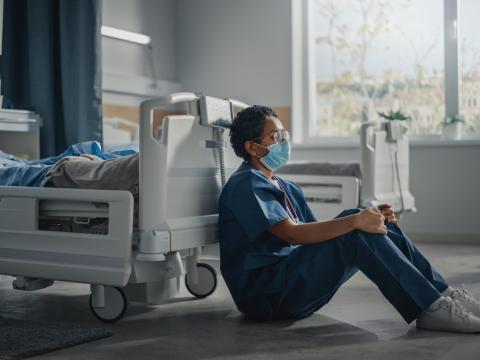 Sad nurse next to empty hospital bed
