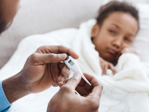 Sick girl in bed with dad taking her temperature
