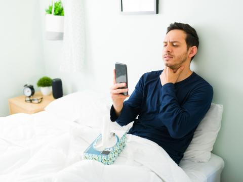 Sick man checking throat in bed