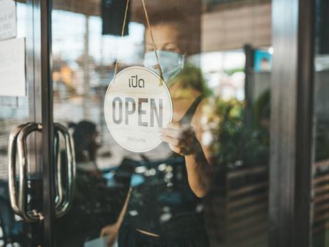 Store owner with mask and "open" sign
