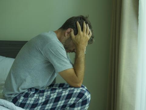 Stressed man sitting on edge of bed