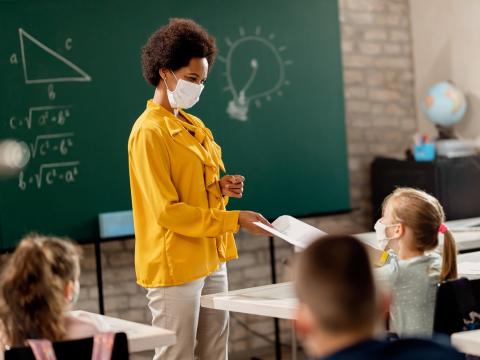 Masked teacher handing out a test