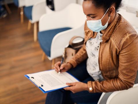 Woman in medical mask filling out healthcare paperwork