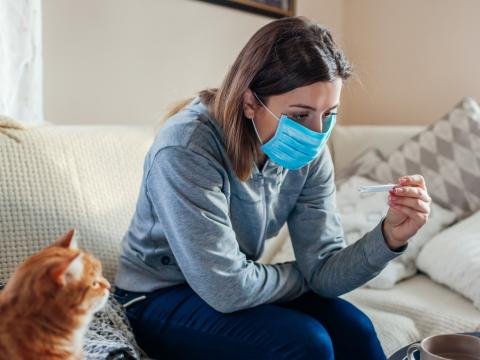 Woman wearing mask at home checking her temperature