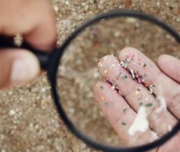 A hand holds a magnifying glass over a palmful of colorful plastic pieces