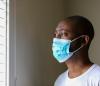 Black man wearing mask looks out window