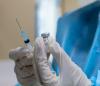 Gloved hands holding COVID vaccine vial and syringe