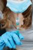 Health worker holding COVID vaccine vial upside down with syringe