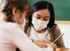 Masked teacher helping masked student