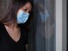 Sad woman wearing mask and her reflection in window