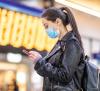 Woman with mask and cell phone at train station